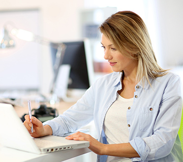 Woman sitting in green chair using laptop in a sunny room